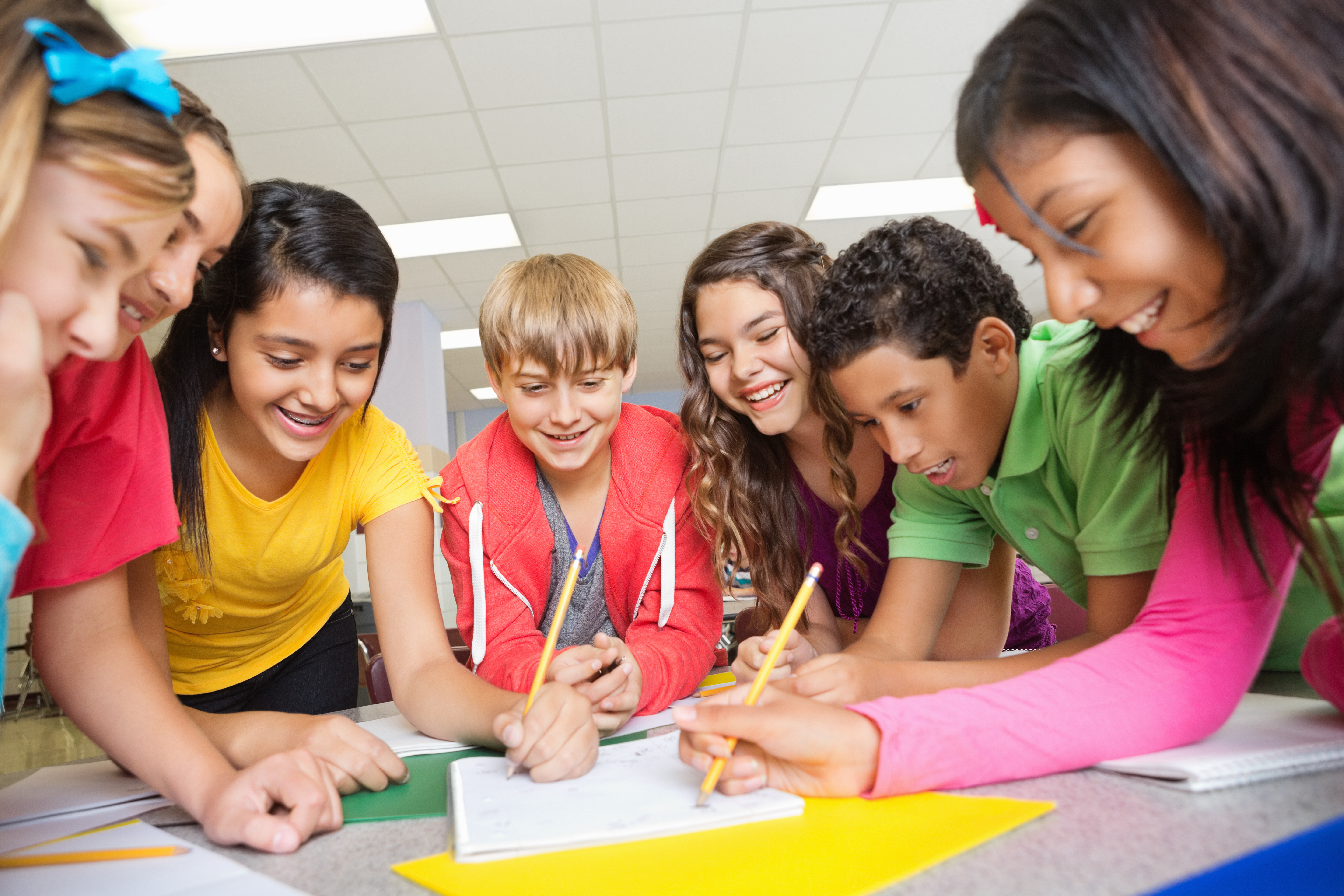 Students are sitting at individual desks in a classroom, writing in notebooks and books.