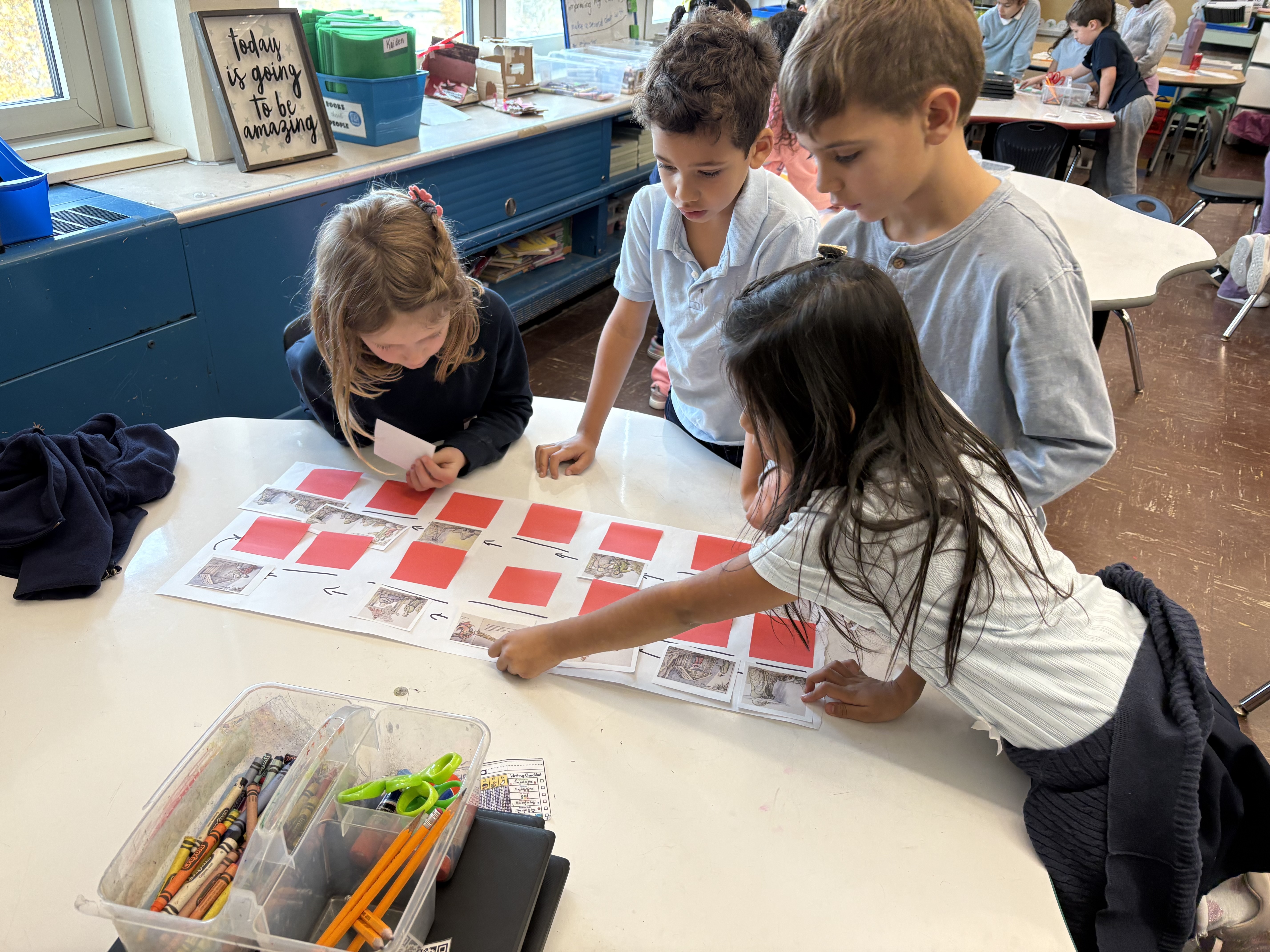 Four young students working at a table on a task. The students appear to be having a discussion.