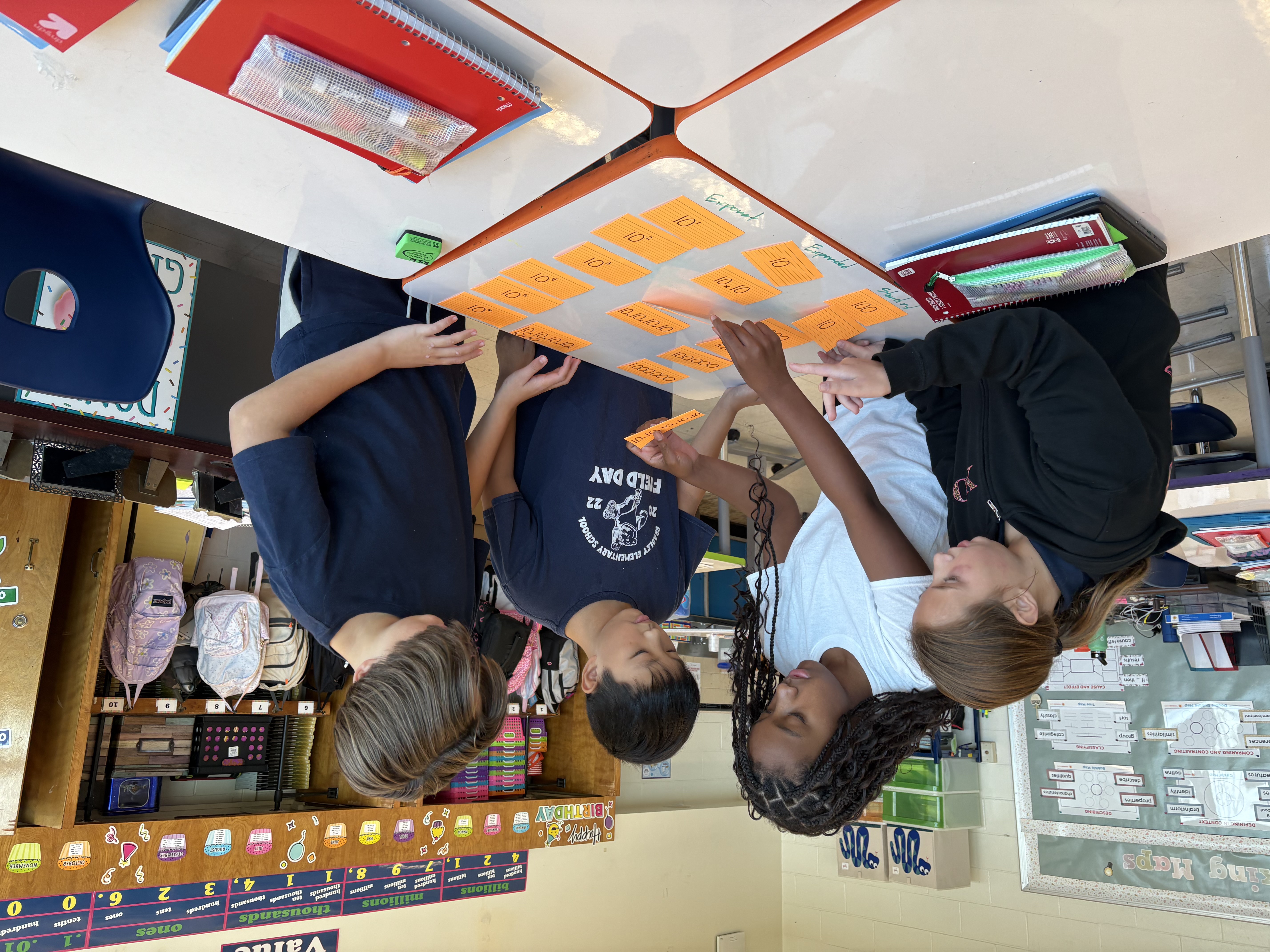 Four older elementary students working together in a group. They are sorting notecards with numbers into three columns.